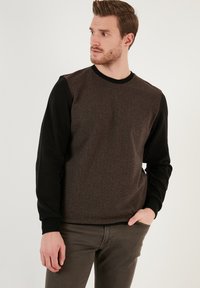 Pullover sweatshirt with a textured brown body and black sleeves, featuring a crew neck and ribbed cuffs. Smooth fabric with horizontal lines.
