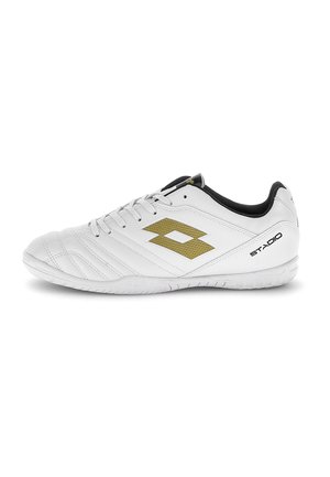 Zapatilla blanca de fútbol sala con forro interior negro, logo dorado en el lateral, cordones blancos y texto "STADIO" cerca del talón en la suela.