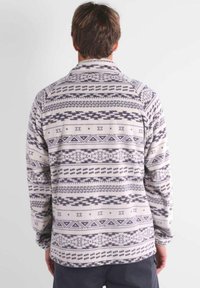 Giacca in pile grigia e bianca con motivi geometrici, maniche lunghe e colletto; texture morbida e vestibilità comoda.