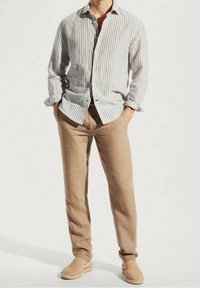 Gestreiftes Hemd mit Knöpfen in Hellbeige und Weiß, kombiniert mit hellbraunen Leinenhosen und beigen Espadrilles, was ein lässiges, entspanntes Erscheinungsbild vermittelt.