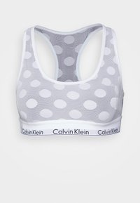 Bralette de malha branca com grandes bolinhas, design de costas nadador e uma faixa com o logótipo da Calvin Klein em preto. Textura suave.