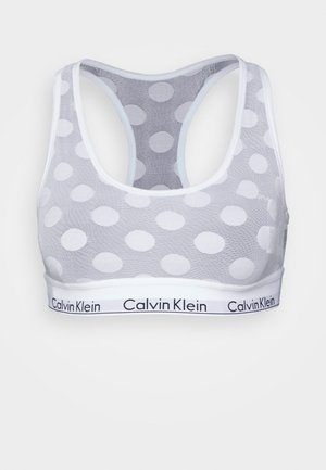 Bralette de malha branca com grandes bolinhas, design de costas nadador e uma faixa com o logótipo da Calvin Klein em preto. Textura suave.
