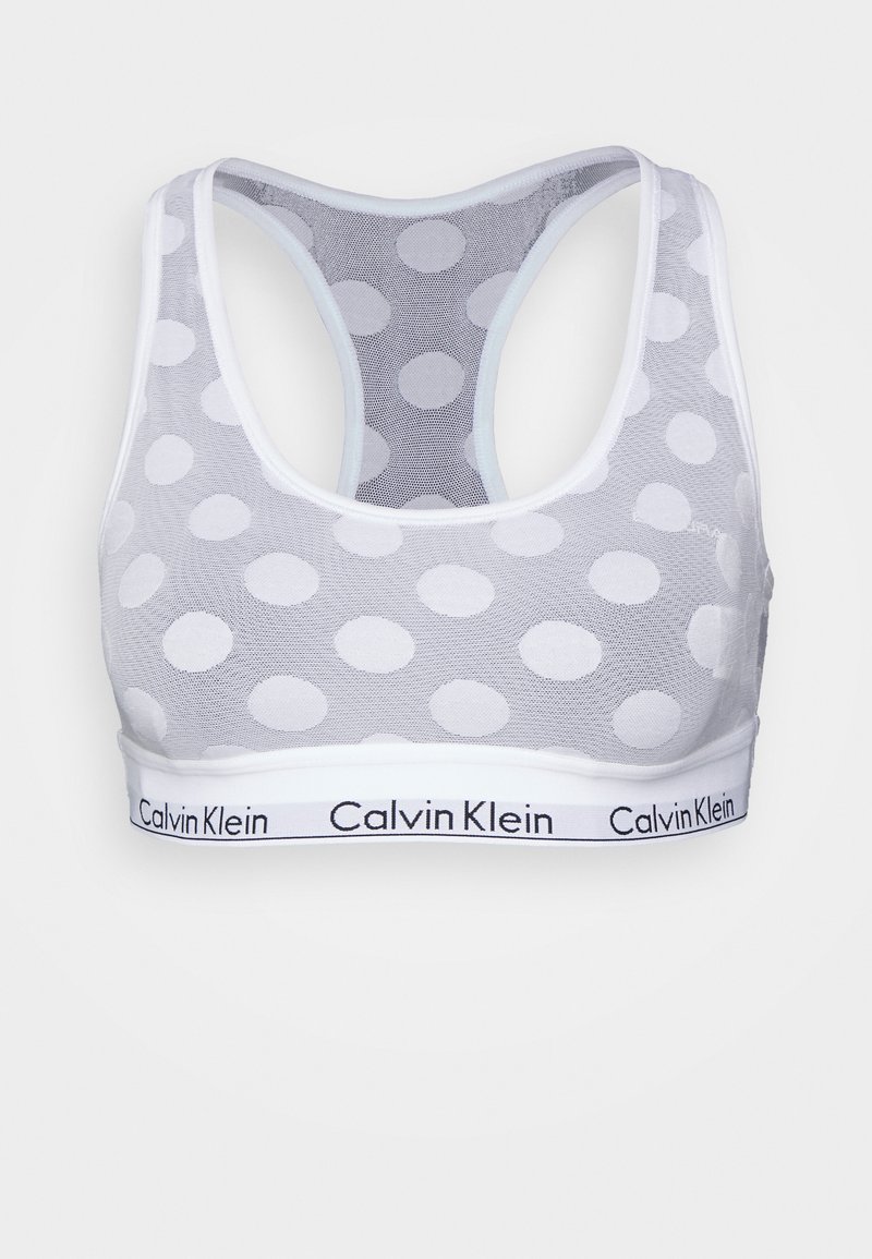 Bralette de malha branca com grandes bolinhas, design de costas nadador e uma faixa com o logótipo da Calvin Klein em preto. Textura suave.