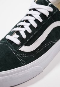 Grüne Wildleder-Sneaker mit weißen Lederakzenten, dicken weißen Schnürsenkeln und einer Gummisohle. Verfügt über kontrastierende Nähte und ein klassisches Design.