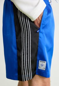 Modré a čierne športové šortky s tromi bielymi pruhmi, bočnou vreckou a logom Adidas s textom "Oficiálny odev".