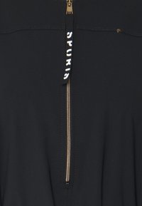 Schwarzes Zip-Top aus glattem Stoff. Mit einem goldenen Reißverschluss und "SPORTS"-Text am Reißverschlussgriff. Einfaches Design mit minimalen Akzenten.