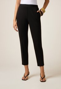 Pantaloni neri, sartoriali, con una vestibilità slim, cintura elastica e tasche laterali. Tessuto liscio con una leggera lucentezza, lunghezza cropped sopra la caviglia.