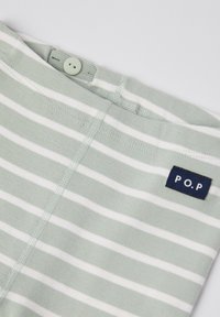 Vihreä raidallinen kangas, jossa on valkoisia viivoja, napin kiinnitys ja tummansininen etiketti, jossa on "P.O.P" vyötäröllä. Pehmeä textura.