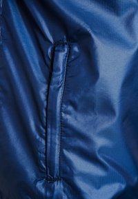 Navy sininen takin kangas, jossa on sileä, kiiltävä pinta ja hienovarainen herringbone-kuvio. Sisältää sivusauman taskun, jossa on ommeltu ääriviiva.