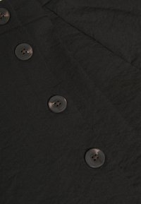 Tela negra con una textura lisa y ligera, con cuatro botones redondos y oscuros cosidos a lo largo del borde.