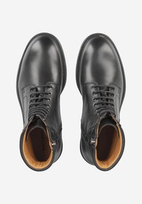 Bottes noires en cuir à la cheville avec une finition lisse, bout rond, design à lacets et doublure intérieure marron contrastante. Fermetures éclair sur les côtés.