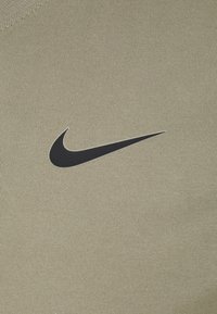 Camisa atlética verde oliva con un tejido texturizado. Presenta un prominente logo de swoosh negro de Nike en el pecho. Diseño simple y ajustado.