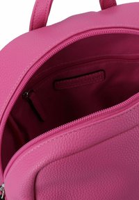 Interiorul unui rucsac din piele texturată roz, dotat cu o pocket cu fermoar și un căptușeală netedă, având un închizător cu fermoar și mânere duale.