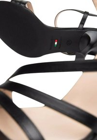Sandal in pelle nera con tacco alto e cinturini, dotata di una soletta nuda liscia. Presenta una suola nera strutturata e un marchio con etichetta Made in Italy.