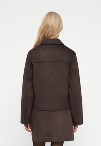 Bruine neplederen suede jacket met een geknipte kraag, lange mouwen en een rechte snit. Zichtbare naaddetails aan de achterkant.