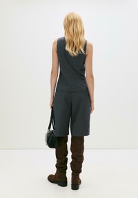 Grå randig ärmlös topp kombinerad med matchande shorts, kompletterad med knähöga bruna mockaskor och en liten svart handväska.