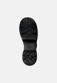 Suola di scarpa in gomma nera caratterizzata da una superficie testurizzata con motivi incrociati per una migliore aderenza, punta arrotondata e design del tacco piatto.
