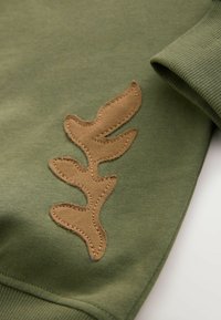 Sweat-shirt vert olive avec motif de feuille beige texturée brodé sur le devant. Présente des poignets côtelés et une texture de tissu lisse.