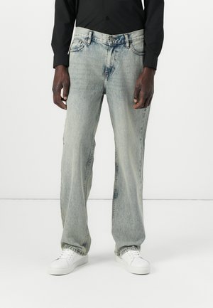Light blue, wide-leg jeans with a faded finish, five pockets, button and zipper closure, and white stitching; worn with white sneakers.
