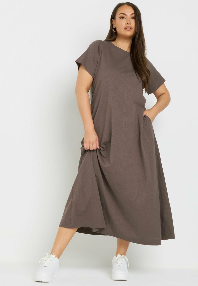 Dunkelgraues, ärmelloses Maxikleid mit Rundhalsausschnitt und Taschen, aus weichem Stoff mit lockerer Passform, kombiniert mit weißen Schuhen.