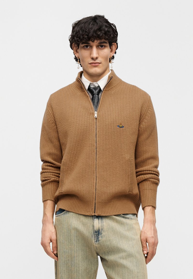 Brown knitted zip-up cardigan with a ribbed texture and a small logo on the left chest. Paired with light blue distressed jeans.