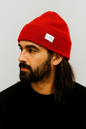 Red, ribbed knit beanie with a folded cuff and a small white label featuring black text. The model has long hair and is wearing a black shirt.