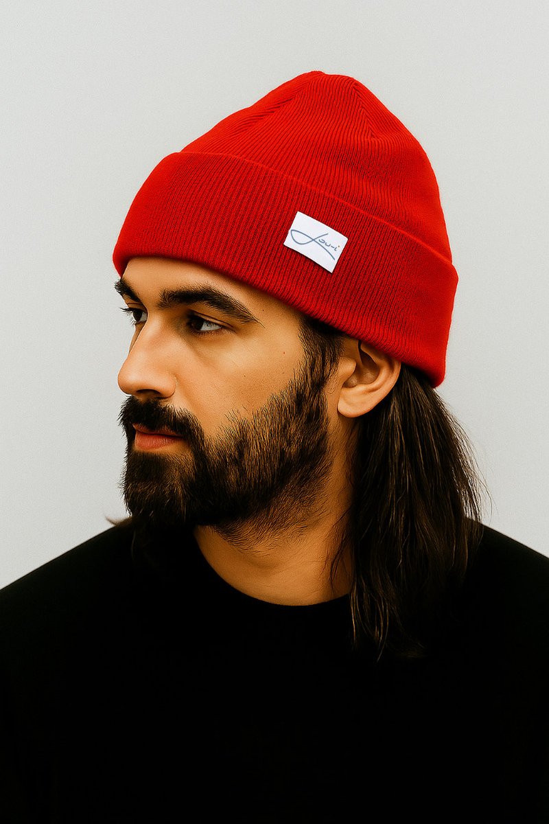 Red, ribbed knit beanie with a folded cuff and a small white label featuring black text. The model has long hair and is wearing a black shirt.