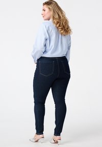 Jean skinny bleu foncé avec poches arrière et détails de couture subtils, associés à une chemise à rayures bleu clair et boutons et des talons argentés.