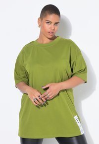 Camiseta de gran tamaño en verde oliva, confeccionada en suave algodón, con mangas cortas, cuello redondo y un detalle de etiqueta en el lateral.