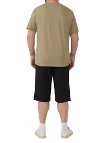 Olijfgroene kortelijnshirt met een ronde hals, gecombineerd met zwarte knielange shorts en witte sneakers met lichtgekleurde zolen.