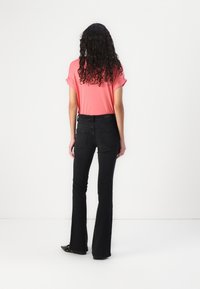 Flared black jeans with a smooth texture, paired with a short-sleeve coral top. The outfit is completed with black flat shoes.