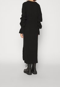 Svart stickad klänning med långa, voluminösa ärmar, rak skärning och sidospår. Kombinerad med svarta snörstövlar.