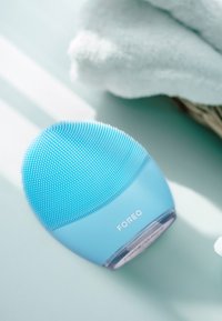 Appareil de nettoyage facial en silicone de couleur bleu vif. Forme arrondie avec une surface texturée pour l'exfoliation. Base transparente avec le logo de la marque.