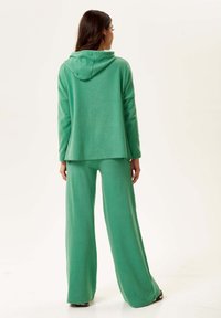 Green loungewear set featuring a hooded sweater and wide-leg pants made of soft fabric, with a relaxed fit and minimal detailing.