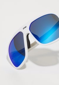 Weiße Sportsonnenbrille mit großen blauen Verlaufslinsen. Der Rahmen ist strukturiert, verfügt über ein Logo an der Seite und flexibles schwarzes Zubehör.