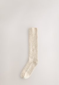 Chaussette beige côtelée avec une texture douce, dotée d'un haut revers et d'un motif chiné subtil, conçue pour le confort et la chaleur.