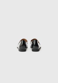 Chaussures en cuir noir avec une finition lisse, un talon bas, un bout arrondi et un design à enfiler avec des côtés ouverts et une doublure intérieure tan.