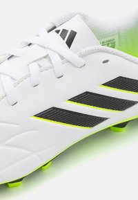 Botas de fútbol blancas con acentos en negro y amarillo fluorescente, que cuentan con bandas laterales texturizadas y una parte superior de cuero suave.
