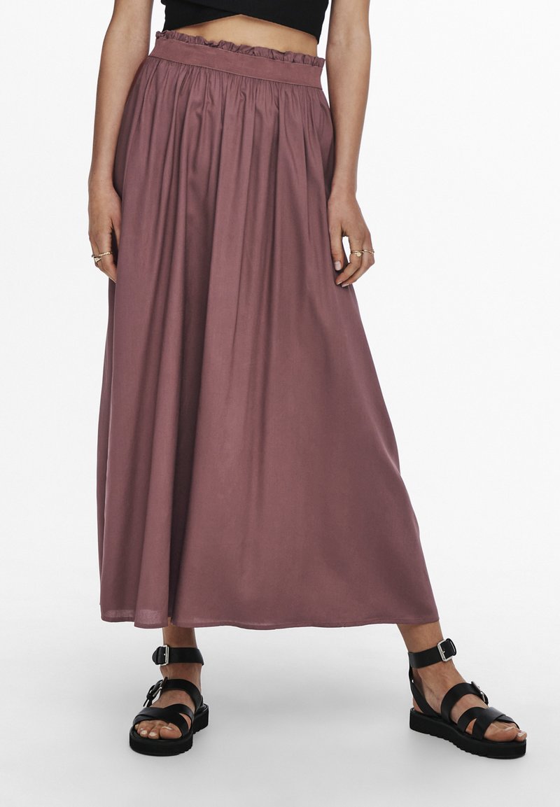 Lang, vloeiende rok van mauve stof met een elastische, ruches tailleband. Gecombineerd met zwarte sandalen met bandjes en een dikke zool.