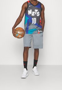 Basketbalový dres s barevným bezrukávovým trikotem, logem "Nets" a šedými šortkami. Obsahuje basketbal, černé ponožky a bílé tenisky.