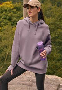 Sweatshirt violet clair avec capuche, manches raglan et ourlet côtelé ; associé à des leggings noirs et une bouteille d'eau transparente violette.