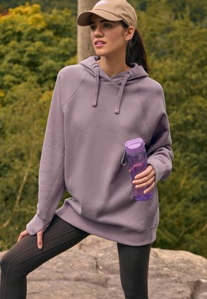 Felpa leggera viola con cappuccio, maniche raglan e orlo a coste; abbinata a leggings neri e una bottiglia d'acqua trasparente viola.