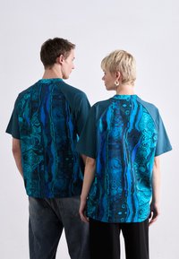 Zwei unisex T-Shirts mit einem blauen und türkisfarbenen abstrakten Muster auf der Rückseite, mit einfarbigen Vorderseiten und lässigen Ärmeln.