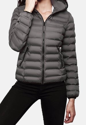 Vrouw draagt een grijze gewatteerde donsjas met een rits aan de voorkant en ritssluitingen aan de zijkanten, gecombineerd met een zwarte broek.