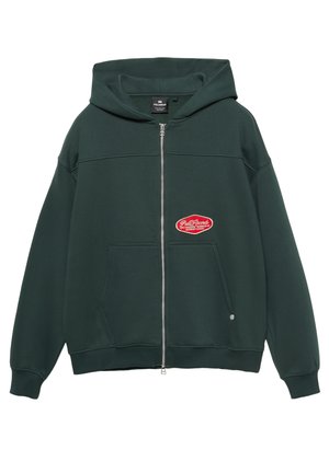 Sweat à capuche zippé vert foncé en tissu doux. Comprend une poche kangourou, des poignets côtelés et un patch logo rouge à l'avant.