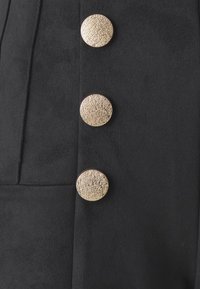Tessuto nero con tre bottoni circolari dorati di texture, con superficie decorata, posizionati verticalmente lungo il lato.