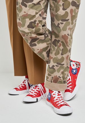 Punaiset kankaiset nilkkurit valkoisilla pohjilla ja nauhoilla. Yhdistetty beigen värisiin camouflage-housuihin ja ruskeisiin leveälahkeisiin housuihin.
