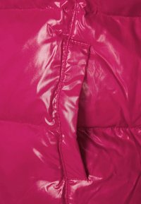 Růžová péřová bunda s lesklým, lesklým povrchem. Má vertikální kapsu na zip a prošívané části pro izolaci.