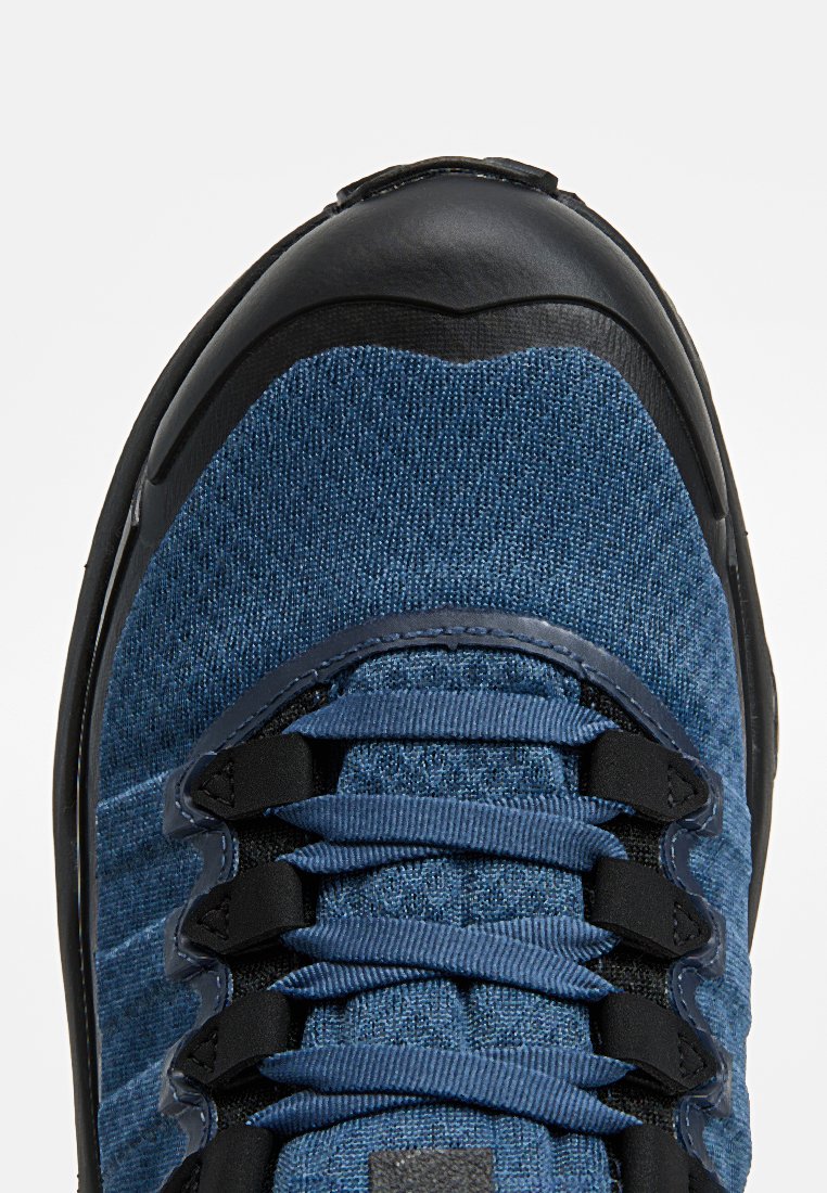 Niebieski tekstylny sneaker z czarną gumową osłoną na palce, z płaskimi sznurowadłami, teksturowanym materiałem i wzmocnionymi obszarami dla zwiększonej trwałości.