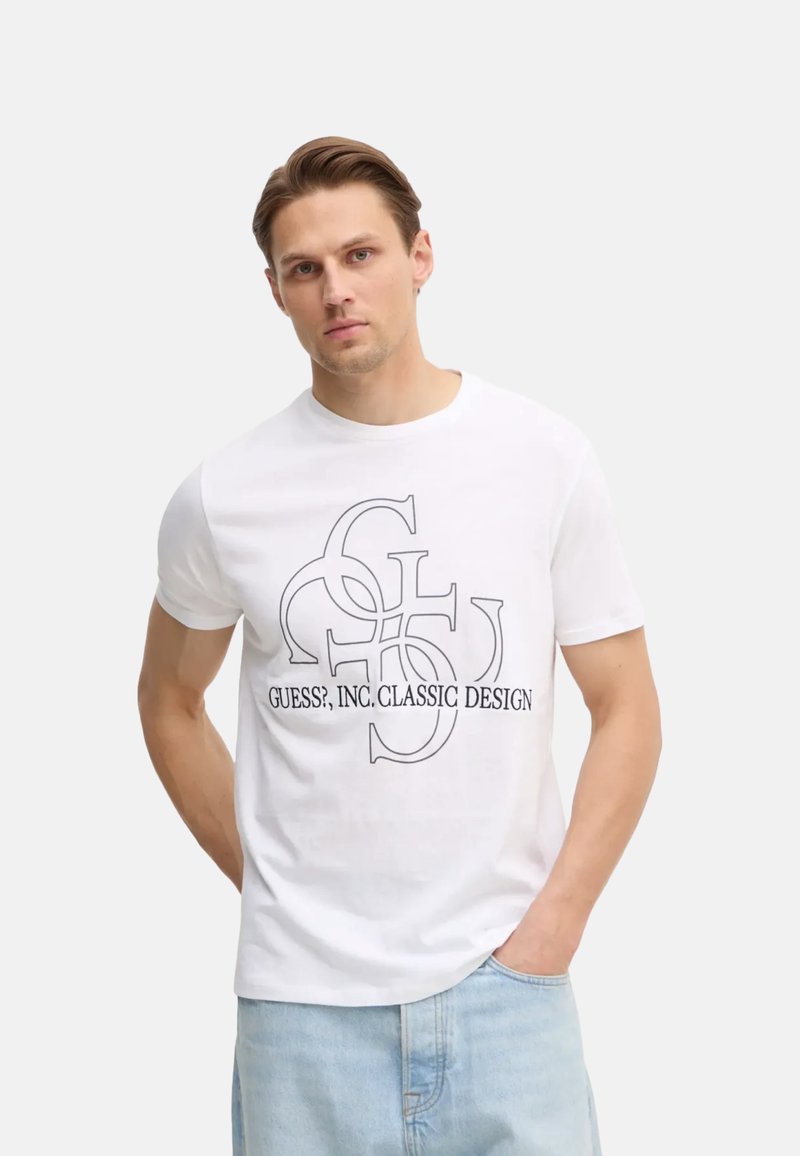 T-shirt bianco a maniche corte con una grafica nera che recita "GUESS?, INC. CLASSIC DESIGN", dalla vestibilità rilassata e colletto girocollo.